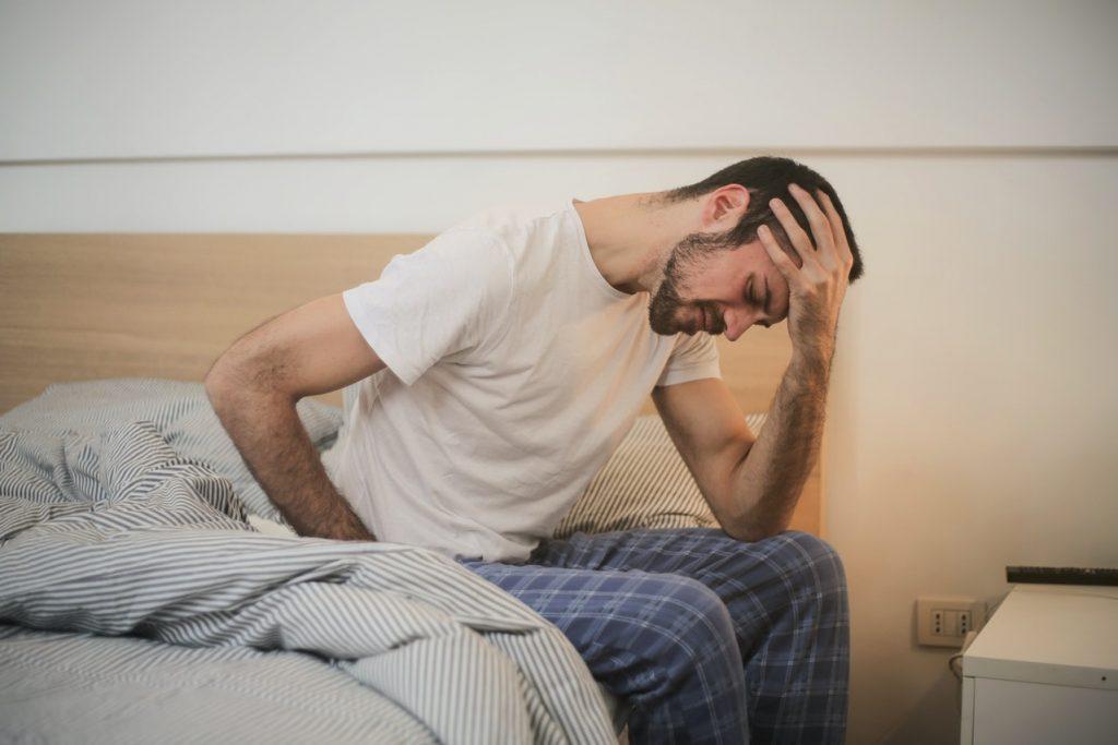 Man sat on a bed suffering from fatigue