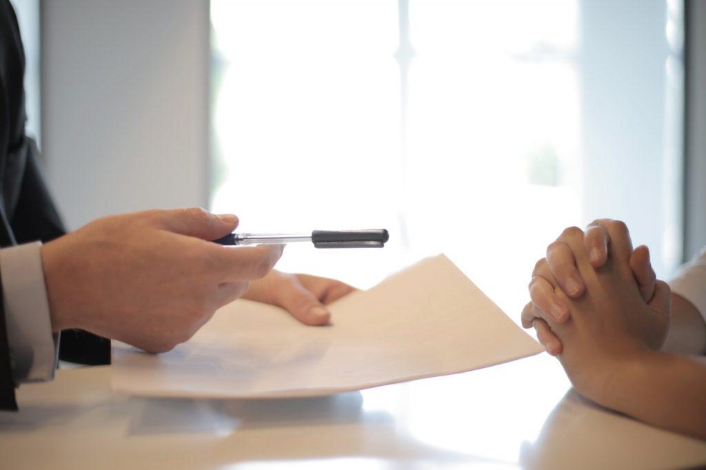 person handing over a contract and pen over to another person