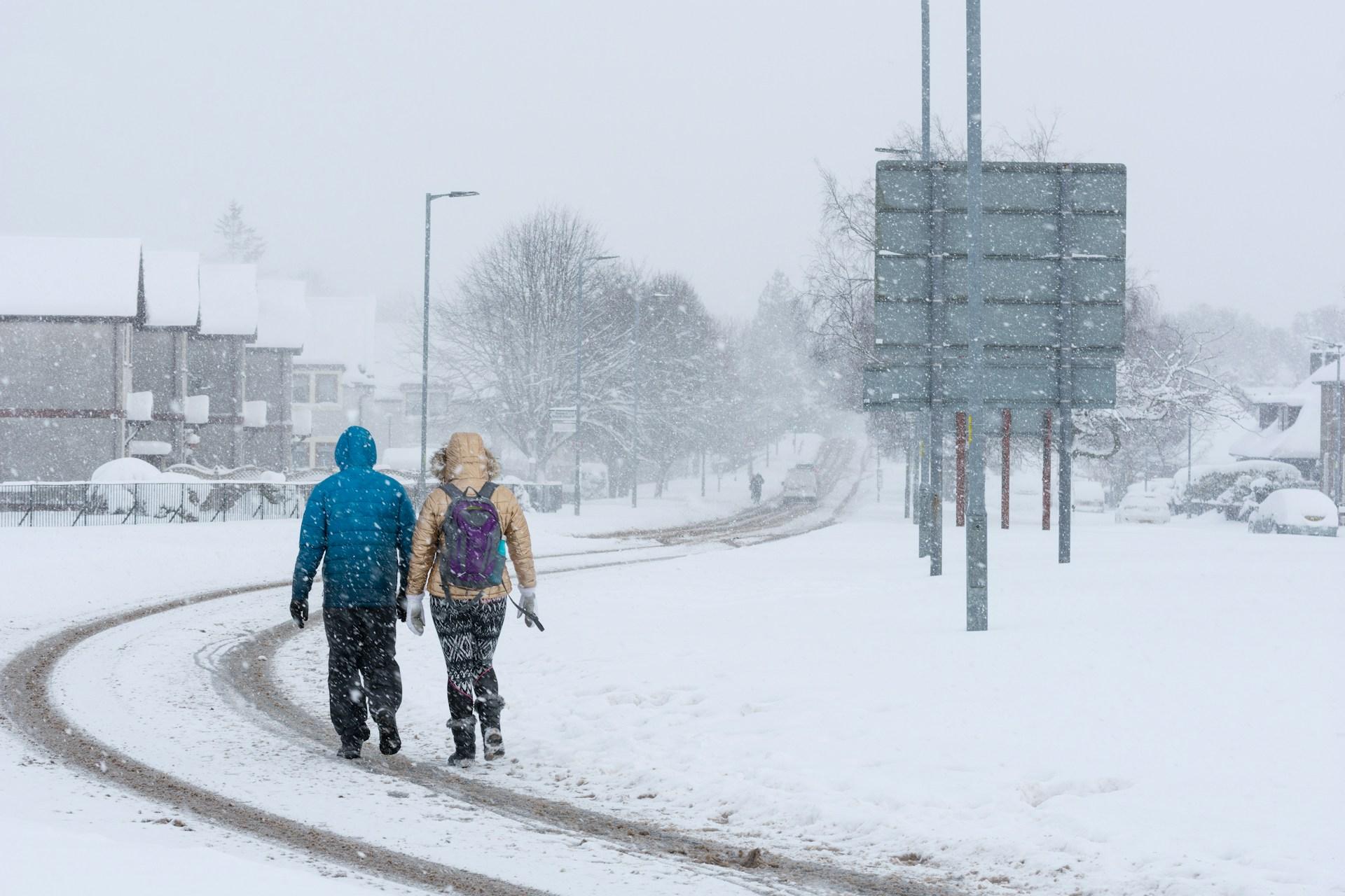 Health and safety in winter weather. Two people walking on a snow covered road